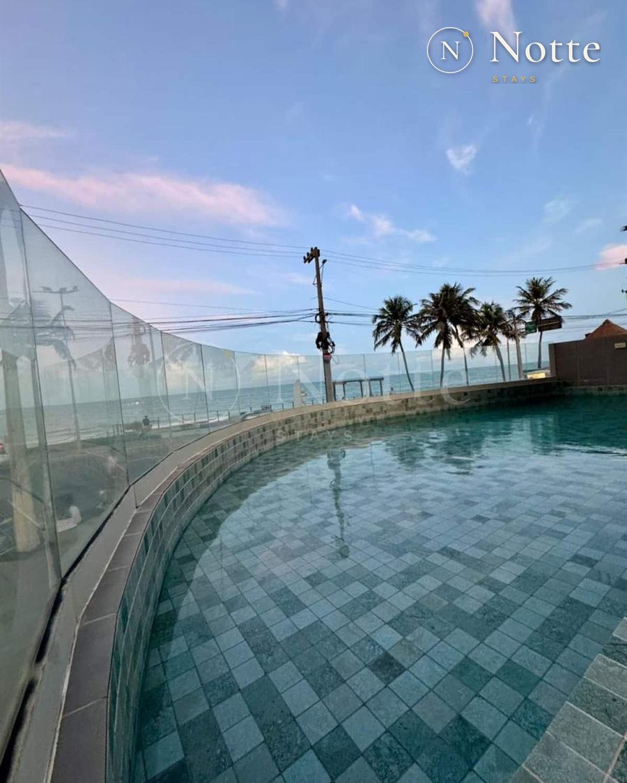 Piscina com borda de vidro e vista para o mar e os coqueiros