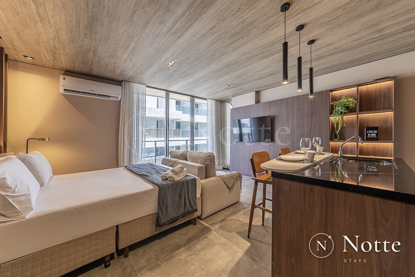 Studio no New Time com cama arrumada, sofá e cozinha com bancada